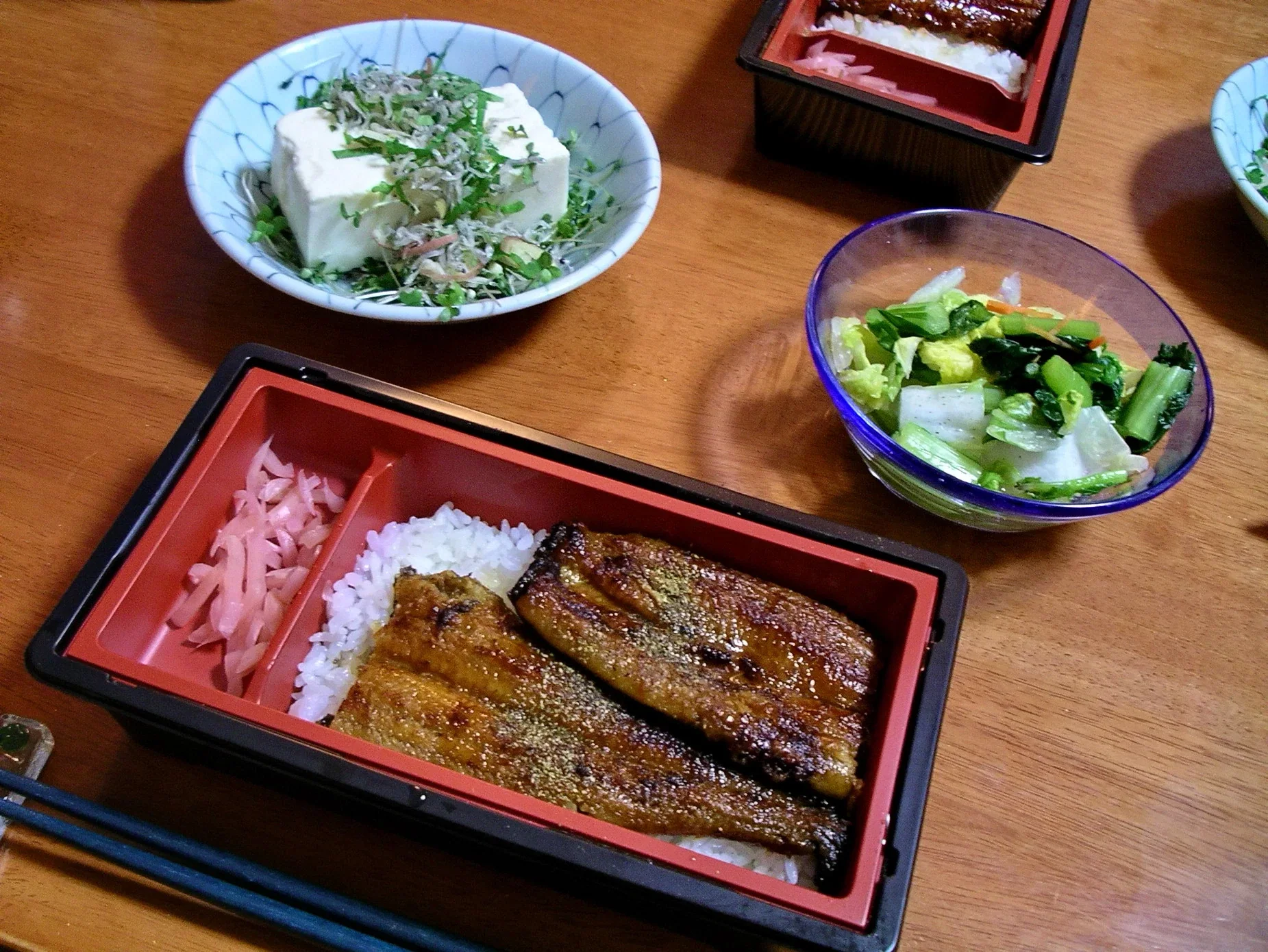 朱紅色漆器便當盒內放著蒲燒鰻魚和白飯,旁邊有冷豆腐與漬物