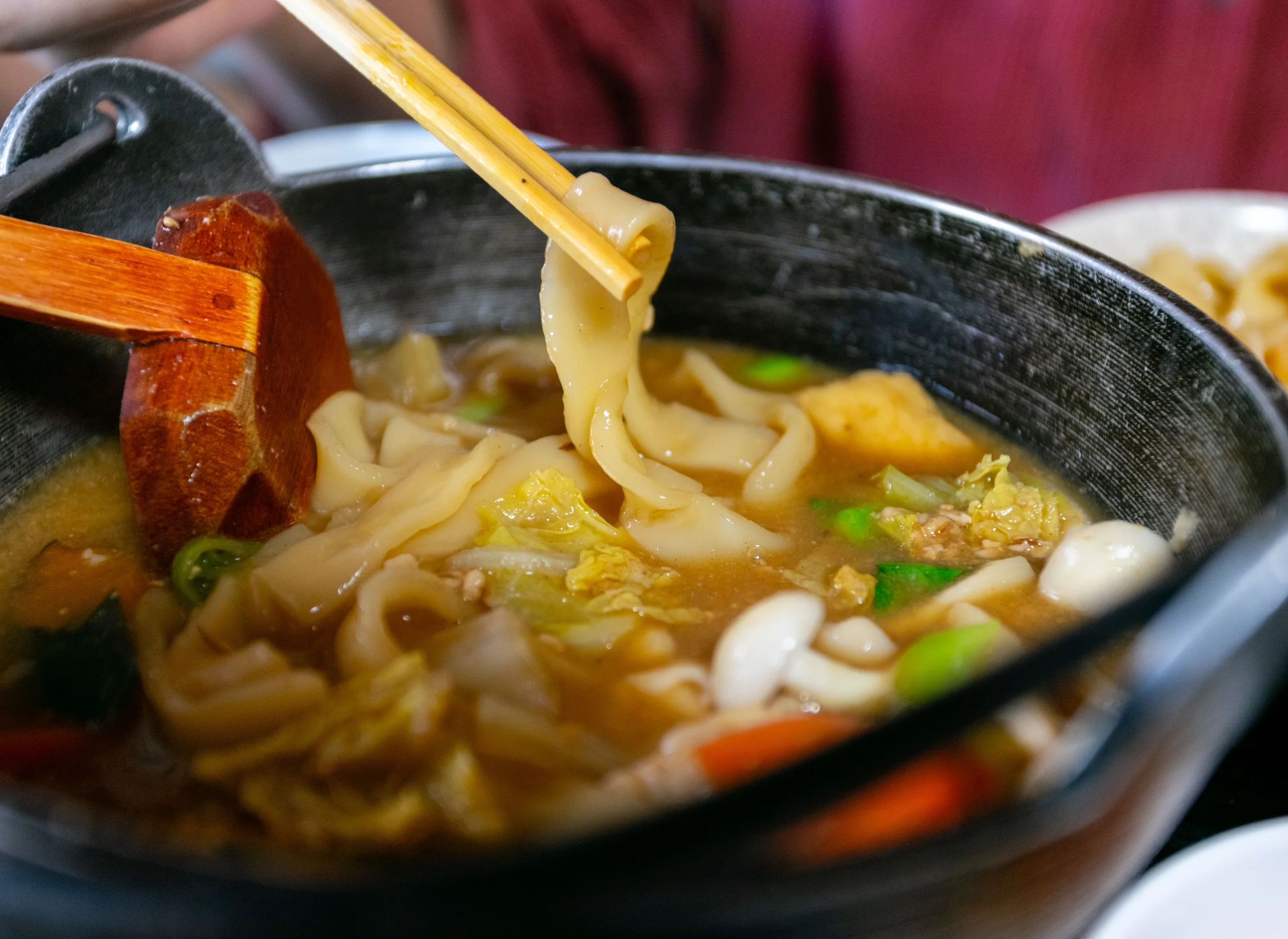 一碗烏龍麵湯麵近照,筷子夾起寬麵