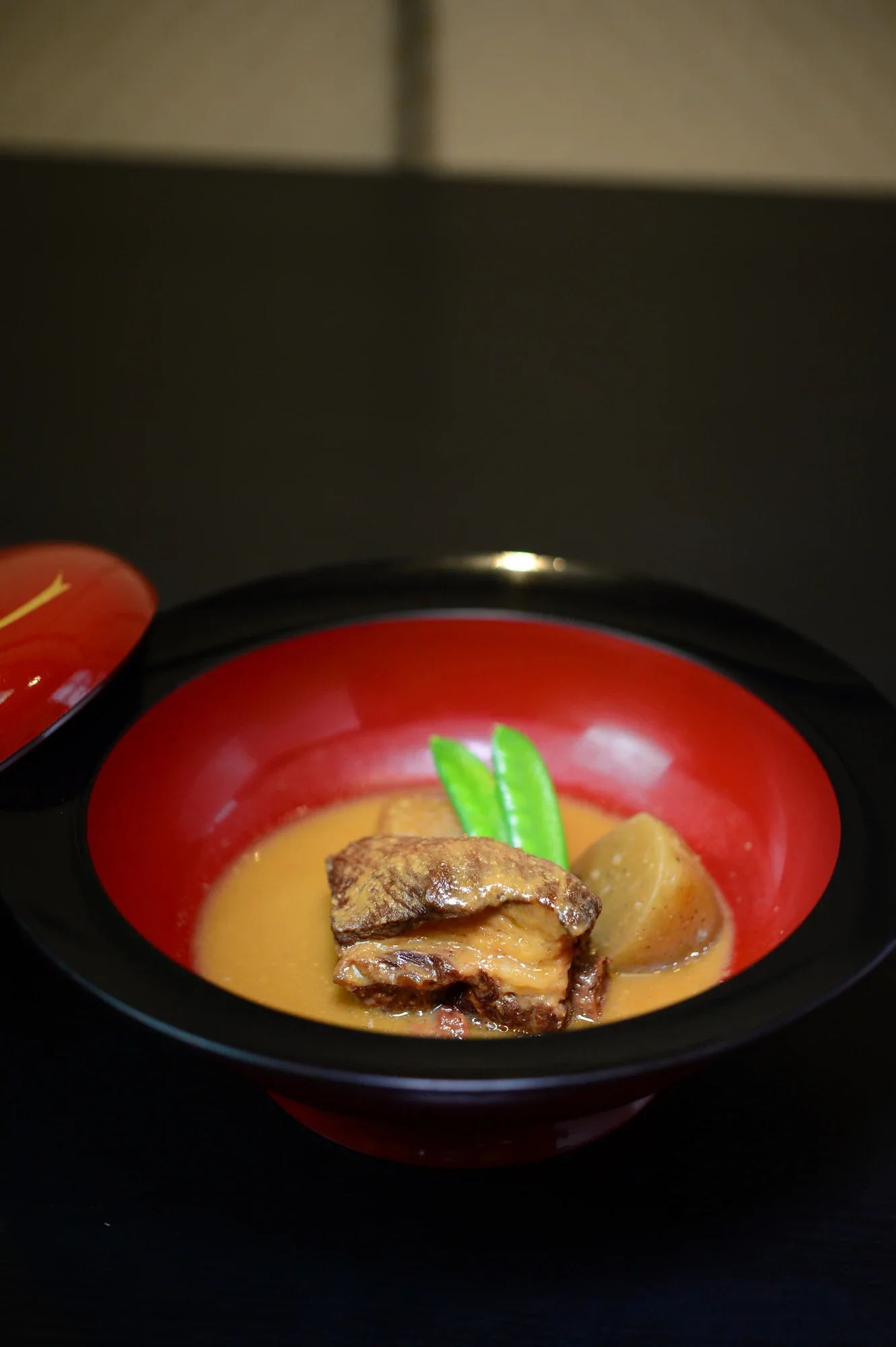 鹿兒島豚骨味噌煮,帶骨豬肉與根菜盛在紅色漆碗中