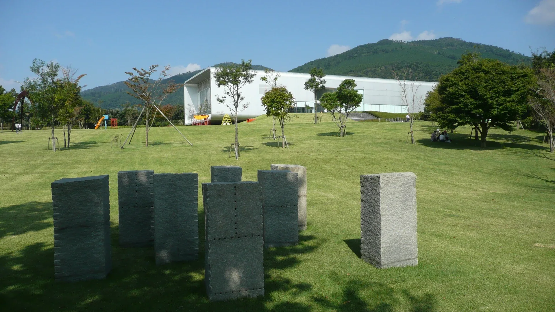 霧島藝術之森戶外草地、作品與白色展館,背景是栗野岳山林