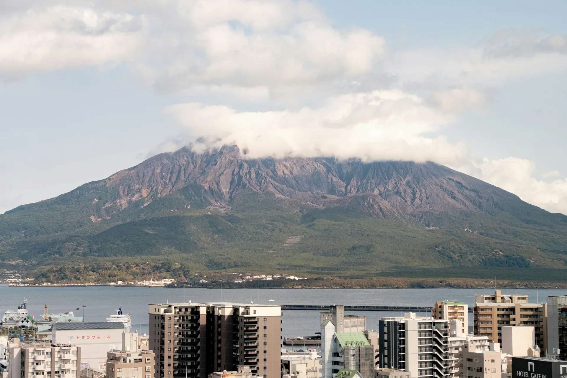 櫻島火山橫跨鹿兒島灣對望市區,前景可見海灣與城市建築