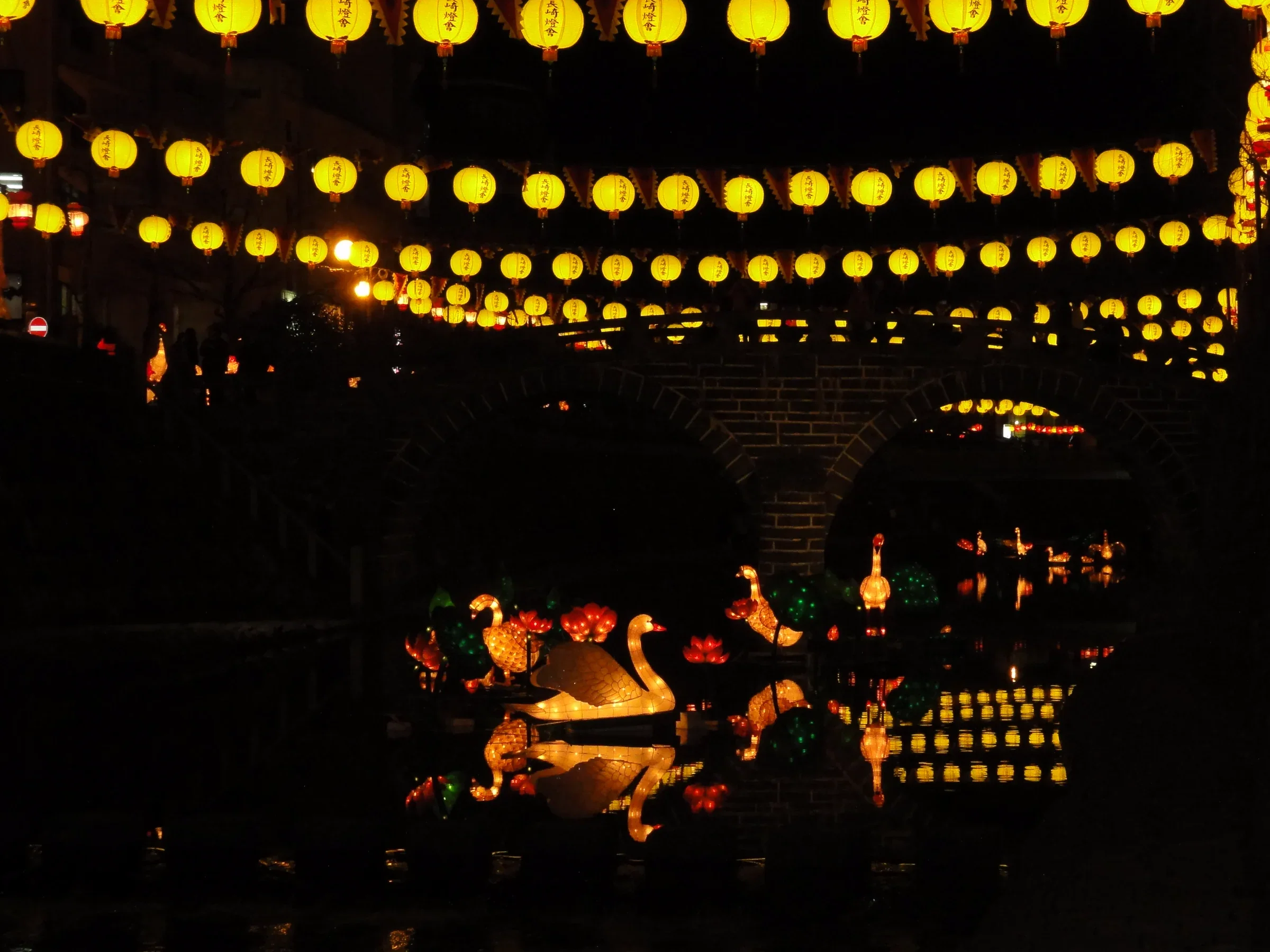 2011 年長崎燈籠節的中島川眼鏡橋夜景，橋上懸掛黃色燈籠，河面有水禽造型燈飾