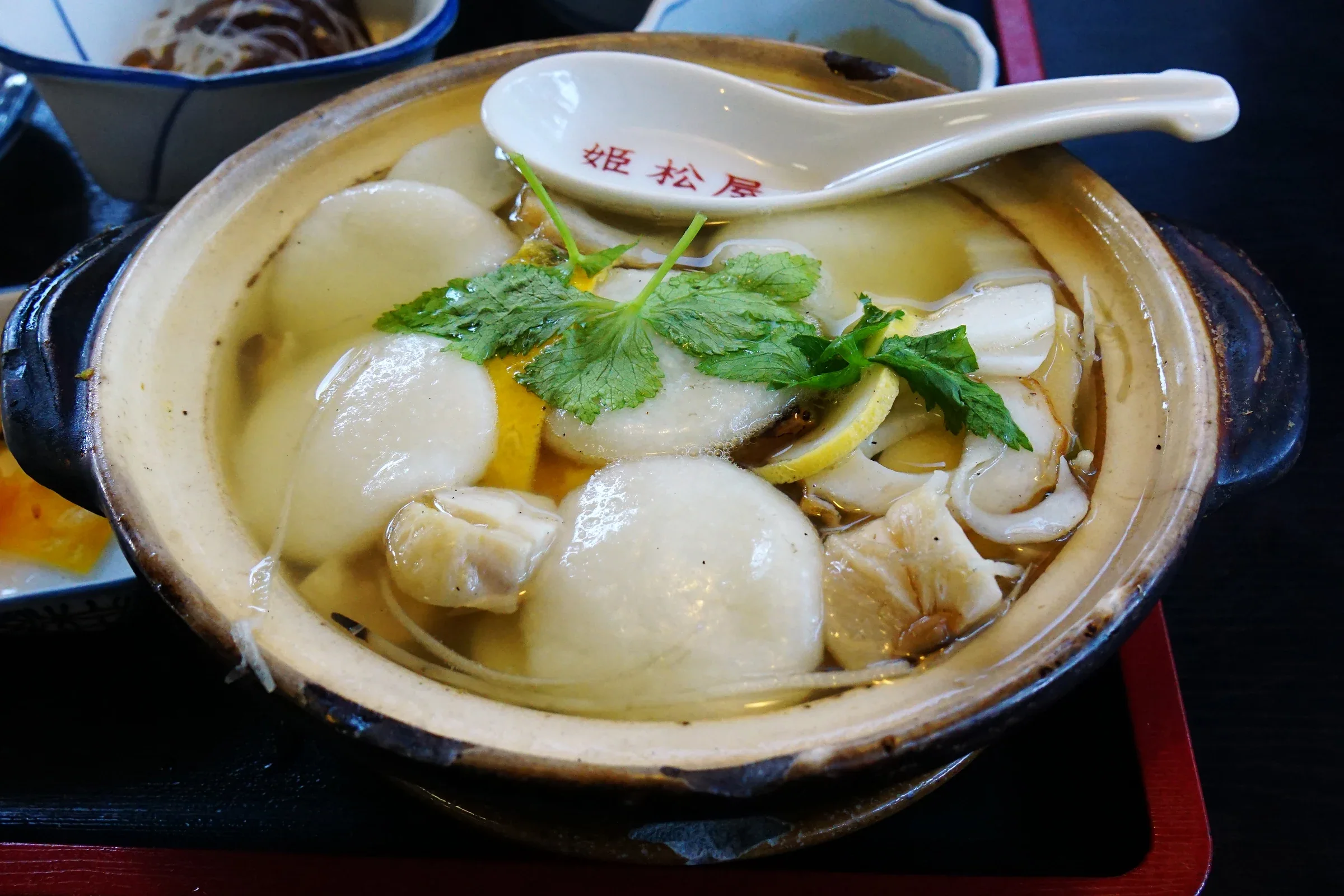 姫松屋本店的島原具雜煮,土鍋內有丸餅、青菜,旁邊放著店名湯匙